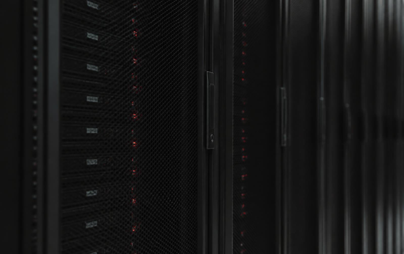Rows of dark server racks with faint red status indicators in a data centre aisle